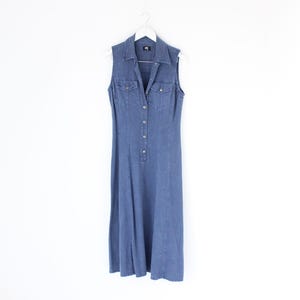 Puede incluir: Un vestido de mezclilla sin mangas con cierre de botones en la parte delantera y cuello. El vestido es de color azul claro y tiene una falda ligeramente acampanada.