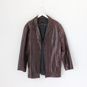 May include: A brown leather jacket with a button closure and a single pocket on the left side.