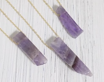 May include: Three gold chains with amethyst crystal pendants. The amethyst crystals are long and narrow, with a purple hue.