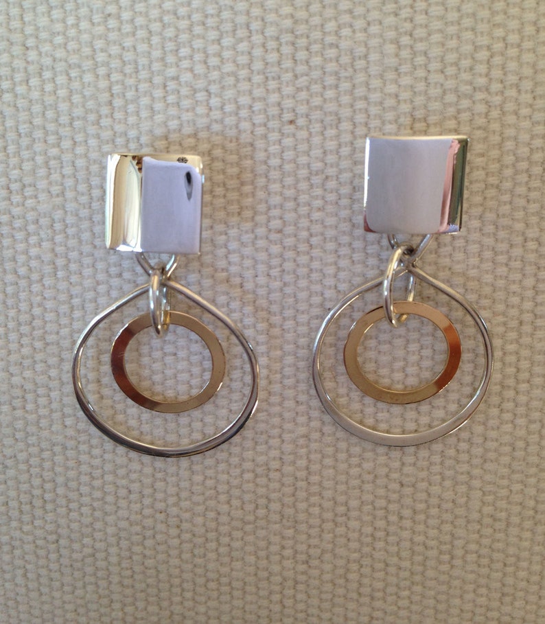 May include: Silver dangle earrings with a square top and two silver circles, one inside the other.