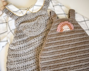 May include: Two crocheted baby dungarees, one with a brown heart and the other with a rainbow. Both dungarees are made with brown yarn.