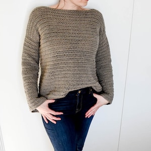May include: A brown crocheted sweater with long sleeves and a boat neck. The sweater is worn over blue jeans.
