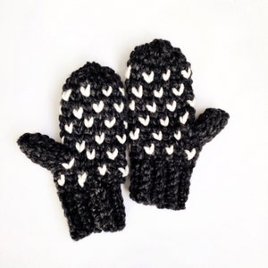 May include: A pair of black and white knit mittens with a heart pattern. The mittens have a thumb and a finger section.