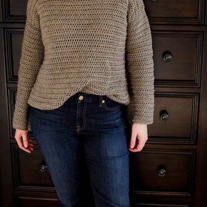 May include: A brown crocheted sweater with long sleeves and a loose fit. The sweater is worn over a pair of blue jeans.
