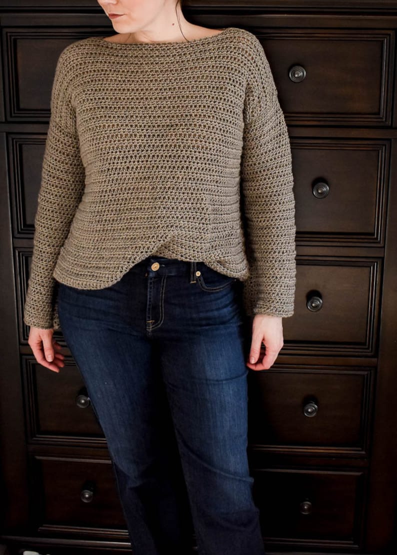 May include: A brown crocheted sweater with long sleeves and a loose fit. The sweater is worn over a pair of blue jeans.