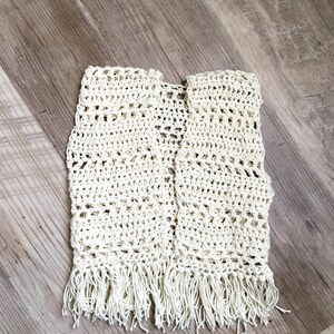 May include: A white crocheted vest with fringe on the bottom.