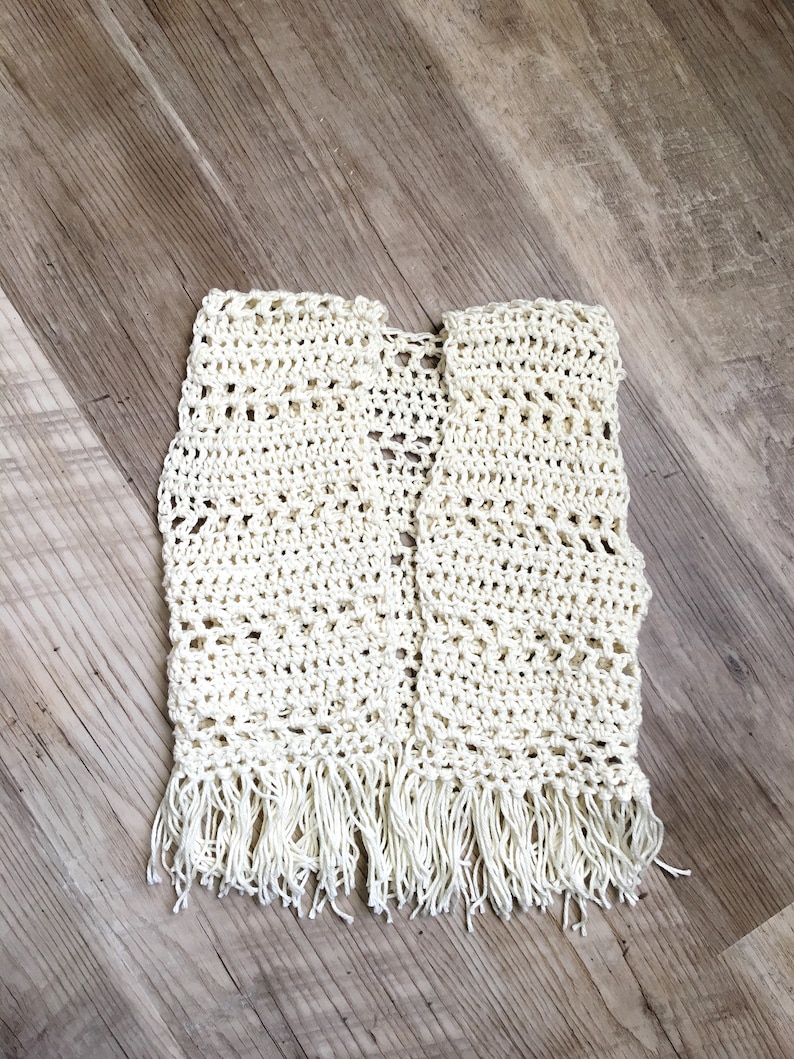 May include: A white crocheted vest with fringe on the bottom.