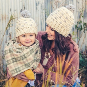 Puede incluir: Una mujer y una ni&ntilde;a con gorros de punto a juego con pompones grises. La mujer lleva un jersey granate y la ni&ntilde;a lleva una bufanda de cuadros y un jersey amarillo.