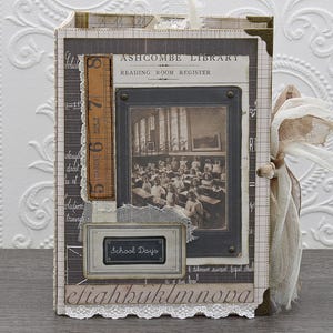 May include: A rectangular journal with a dark brown cover featuring a vintage black and white photograph of a classroom, the text Ashcombe Library Reading Room Register, a brown ruler strip, a School Days label, and white lace trim on the edges.