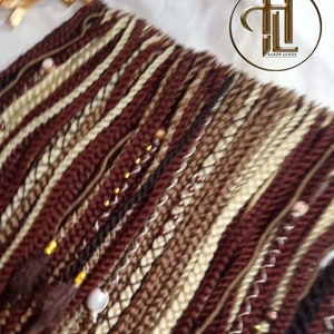 May include: A close-up of a set of brown, beige and white braided hair extensions with gold and brown beads. The extensions are arranged in a fan shape and have a variety of textures.