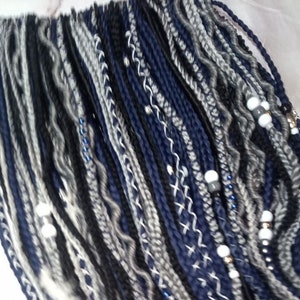 May include: A collection of blue, black and grey synthetic hair extensions with white beads. The hair extensions are braided and have a variety of textures.