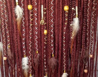 May include: A set of long, maroon dreadlocks with gold and white beads, feathers, and charms. The dreadlocks are arranged in a row and are hanging down.
