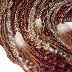 Pode incluir: Uma coleção de dreadlocks sintéticas marrons, loiras e bordô com contas douradas e penas.