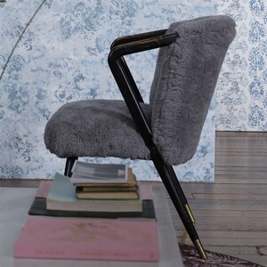 May include: A gray sheepskin chair with black metal legs and gold accents. The chair is sitting on a wooden floor in front of a blue and white patterned wall.