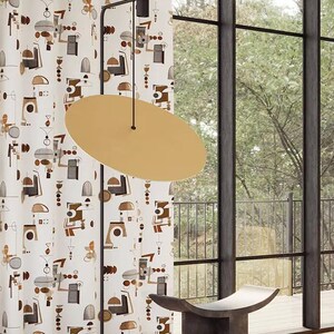 以下が含まれることがあります： 大きな窓と柄物のカーテンを備えたモダンなリビングルーム。 黄色のソファ、金色の楕円形のランプ、濃い灰色のスツール、お揃いの円筒形のサイドテーブルがあります。 カーテンには、繰り返される抽象的なデザインがあります。