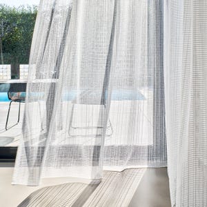 May include: Semi-transparent white curtains with a striped pattern hang in front of a window. The curtains allow light to filter through. The outdoor scene includes a table and chairs near a pool.