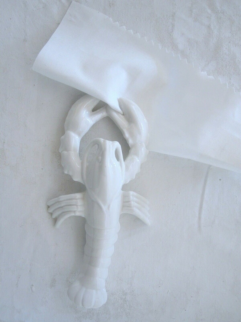 Peut inclure: Figurines de homard en porcelaine blanche avec des griffes et un corps d&eacute;taill&eacute;s. La figurine est pos&eacute;e sur une surface blanche.