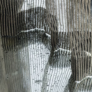 May include: A sheer brown curtain with a striped pattern hangs in front of a window. The curtain is translucent, allowing light to shine through. The curtain is reflected in the window, creating a striped pattern on the glass.