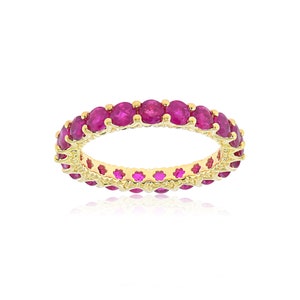 May include: A gold band ring with a row of round, pink ruby stones.