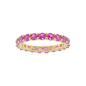 May include: A gold band ring with a row of pink gemstones set in a continuous circle.