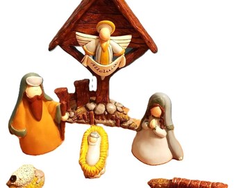 May include: A ceramic nativity scene with a brown wooden stable, a yellow angel with the word "Alleluia" on a banner, a green-robed Joseph, a blue-robed Mary, a baby Jesus in a manger, and two white sheep.