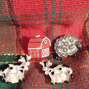 May include: A collection of farm-themed figurines, including two cows with black spots, a red barn, and a sheep with a black face. The figurines are set against a red and green plaid background.