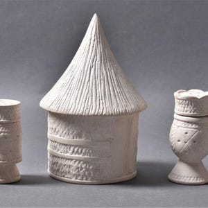 May include: Set of five white ceramic figurines, including a hut with a thatched roof, a tall cylindrical figure, a shorter cylindrical figure, a goblet-shaped figure with a crown, and a triangular figure with a pointed top.