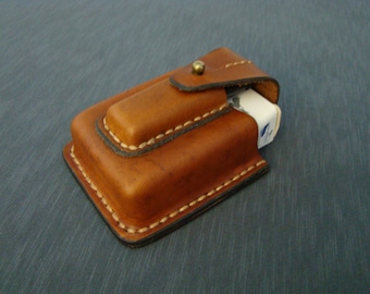 May include: A brown leather cigarette case with a flap and a brass button closure. The case is stitched with white thread and has a worn look.