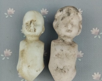 May include: Two vintage porcelain doll heads with no bodies. The heads are white with a slightly off-white color and have a distressed look. The heads are missing paint in some areas and have dirt and grime on them.
