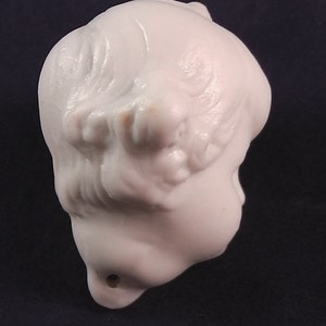 May include: White ceramic figurine of a person's head with long hair. The figurine is smooth and has a hole in the bottom.