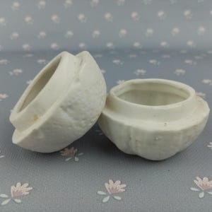 Könnte beinhalten: Zwei weiße Keramikbehälter in Form von halbierten Zitronen. Die Behälter haben eine strukturierte Oberfläche und sind oben offen.