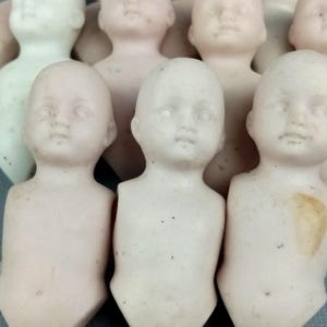 Puede incluir: Un grupo de cabezas de muñecas de porcelana vintage con rasgos pintados. Las muñecas son de color rosa claro y les faltan los cuerpos.