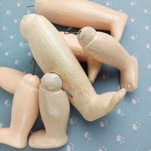 Puede incluir: Colección de piernas de muñeca vintage en varios tamaños y estados de desgaste. Las piernas están pintadas en un tono de piel pálido, algunas muestran signos de edad, incluyendo pintura agrietada. Alambre de metal está unido a la parte superior de cada pierna.