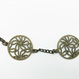 Könnte beinhalten: Eine goldene Kettenkette mit drei runden Anhängern mit einem filigranen floralen Ausschnitt.