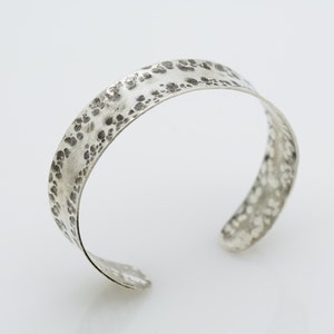 May include: A silver hammered cuff bracelet with a textured surface.