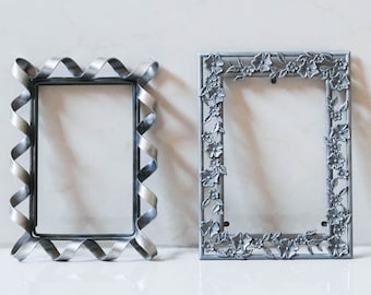 May include: Two silver picture frames, one with a simple, wavy design and the other with a floral design.