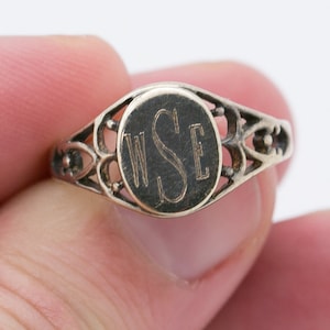 Op de afbeelding: Een zilveren ring met een ovale bovenkant met de gegraveerde initialen "WSE". De ring heeft een delicaat, filigraan ontwerp.
