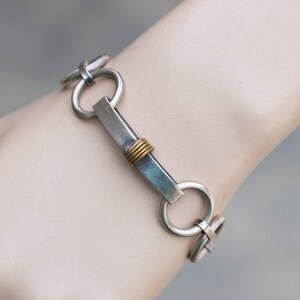 May include: A silver bracelet with a rectangular silver bar and a gold accent. The bracelet is made of linked circles.