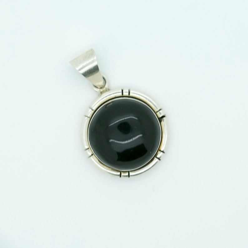 May include: A silver pendant with a black oval gemstone set in a silver bezel. The pendant has a simple design with a smooth finish.