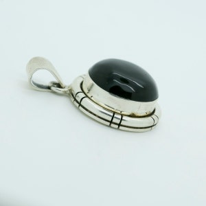 May include: A silver pendant with a black gemstone set in a bezel setting. The pendant has a detailed design around the stone.