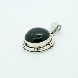 May include: A silver pendant with a black gemstone set in a silver bezel. The pendant has a detailed silver design around the gemstone.