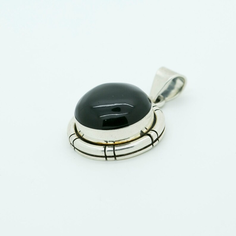 May include: A silver pendant with a black gemstone set in a silver bezel. The pendant has a detailed silver design around the gemstone.
