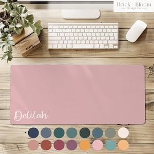May include: A rectangular desk mat in a solid dusty rose color featuring the name Delilah printed in white script lettering on the bottom left corner. Below the mat, sixteen circular color swatches are arranged in two rows.