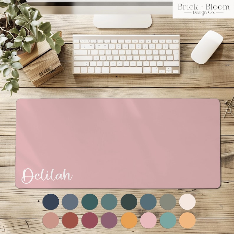 May include: A rectangular desk mat in a solid dusty rose color featuring the name Delilah printed in white script lettering on the bottom left corner. Below the mat, sixteen circular color swatches are arranged in two rows.