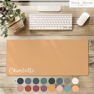 Op de afbeelding: Een rechthoekige, perzik kleurige bureaumat met de naam "Charlotte" in witte letters. De mat ligt op een houten bureau met een toetsenbord, muis en plant. Een kleurenpalet van verschillende tinten wordt eronder weergegeven. De tekst "Brick Bloom Design Co." staat in de rechterbovenhoek.