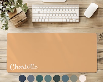 May include: A rectangular desk mat in a solid light orange color featuring the name Charlotte printed in white script font. Below the mat are sixteen small circular color swatches in various shades including blue, green, red, pink, and tan.