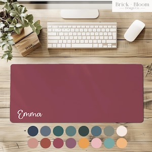 May include: A rectangular desk mat in a solid deep maroon color featuring the name Emma printed in white script lettering on the bottom left corner. Below the mat are sixteen small circular color swatches in various shades.