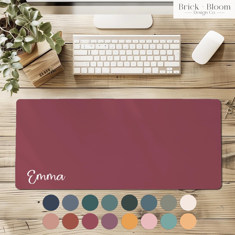 May include: A rectangular desk mat in a solid deep maroon color featuring the name Emma printed in white script lettering on the bottom left corner. Below the mat are sixteen small circular color swatches in various shades.
