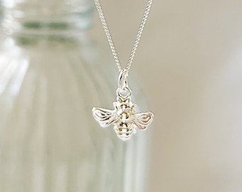 May include: A silver chain necklace with a small silver bee charm pendant. The necklace is hanging from a white background.