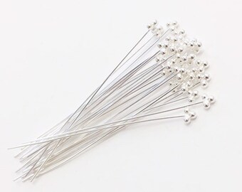 May include: A bundle of silver-toned head pins with small round balls on the ends. The pins are arranged in a fan shape.